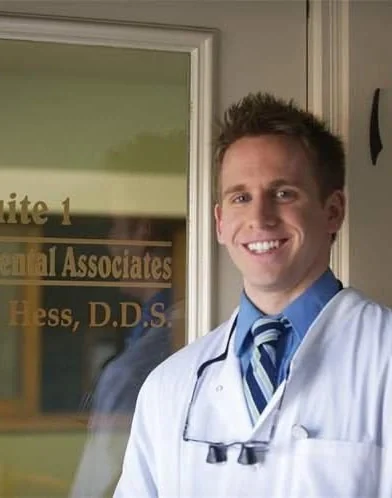 Dr. Michael A. Hess, DDS, smiling in a white coat at the door of his practice.