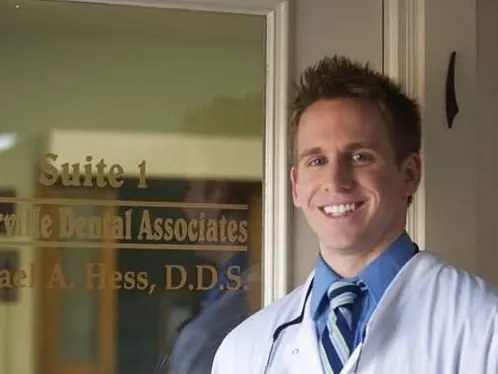 Dr. Michael Hess in a white coat beside the lettered glass door of Suite 1.